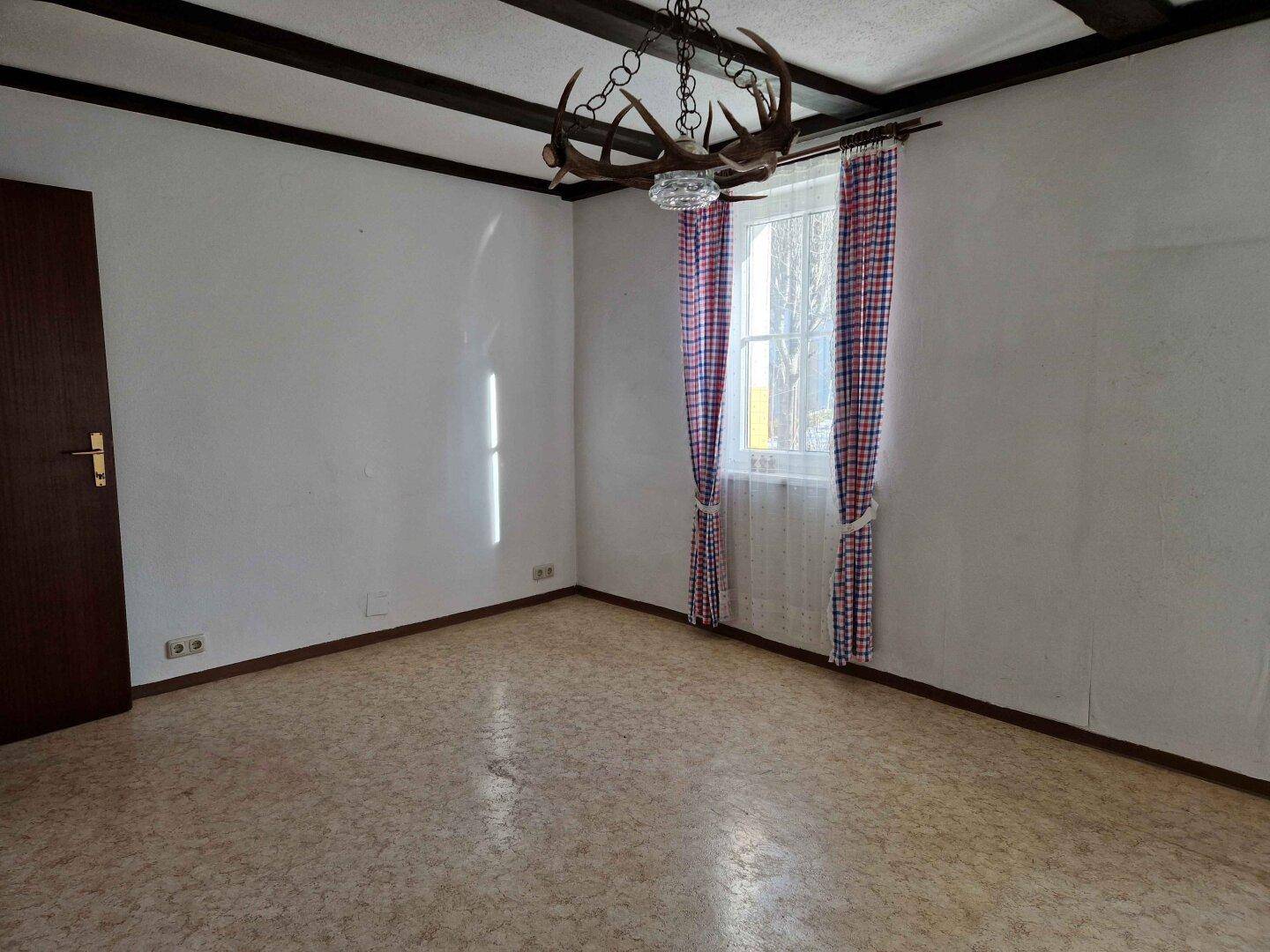 Leeres Zimmer mit Holzbalkendecke und traditionellem Geweih-Kronleuchter.
