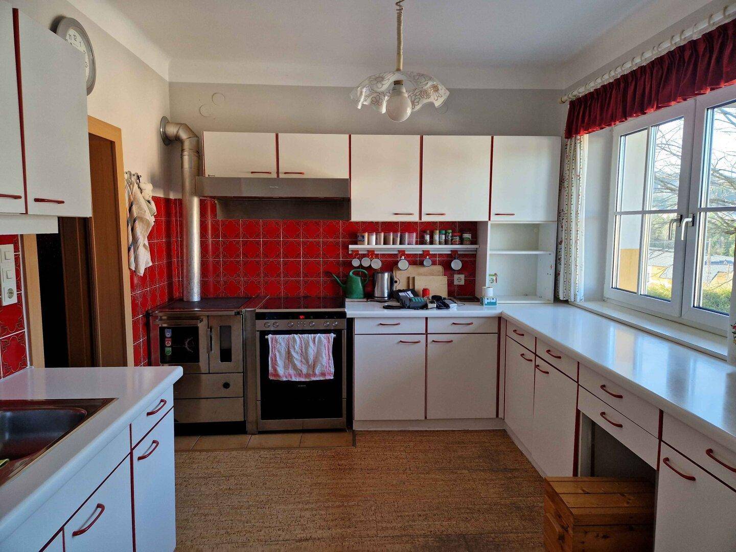 Traditionelle Küche mit weißen Schränken, roten Fliesen und Holzofen.