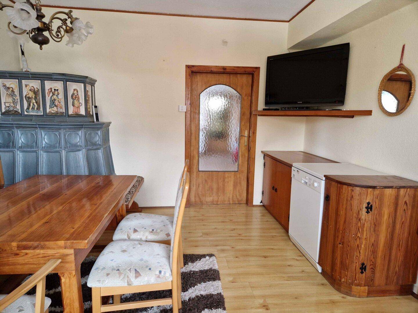 Essbereich mit Holztisch, Kachelofen und integriertem Geschirrspüler.