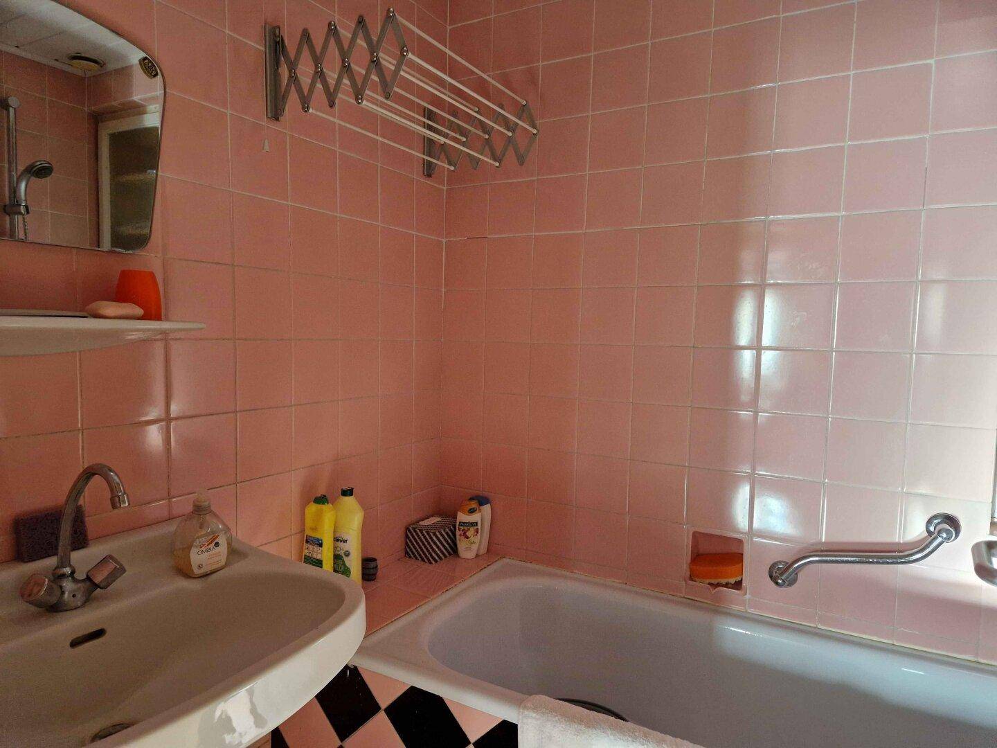 Badezimmer im 80er-Jahre-Stil mit rosa Fliesen und schwarz-weißem Schachbrettmuster.