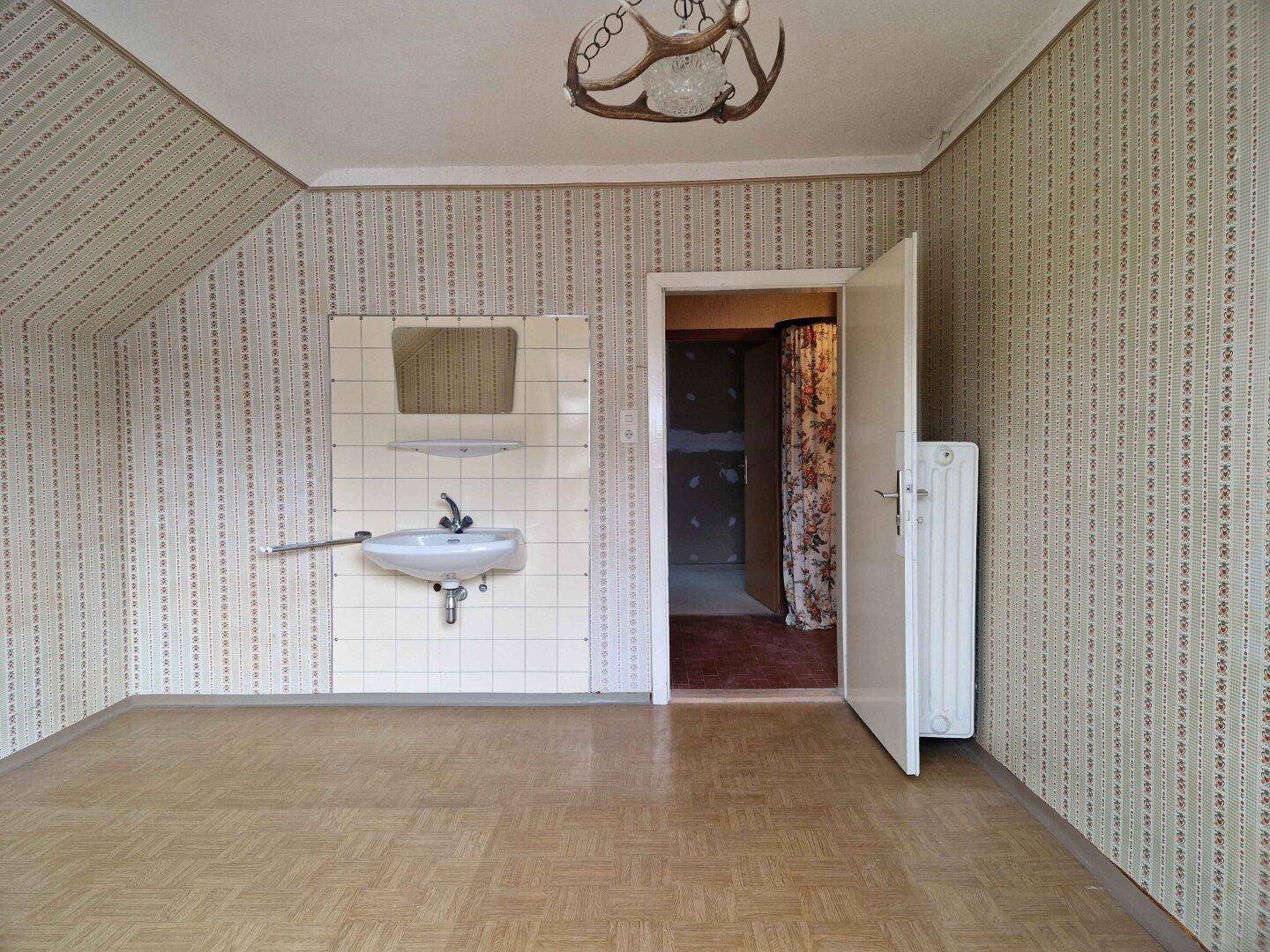 Leeres Zimmer mit gemusterter Tapete, Waschbecken und Dachschräge.