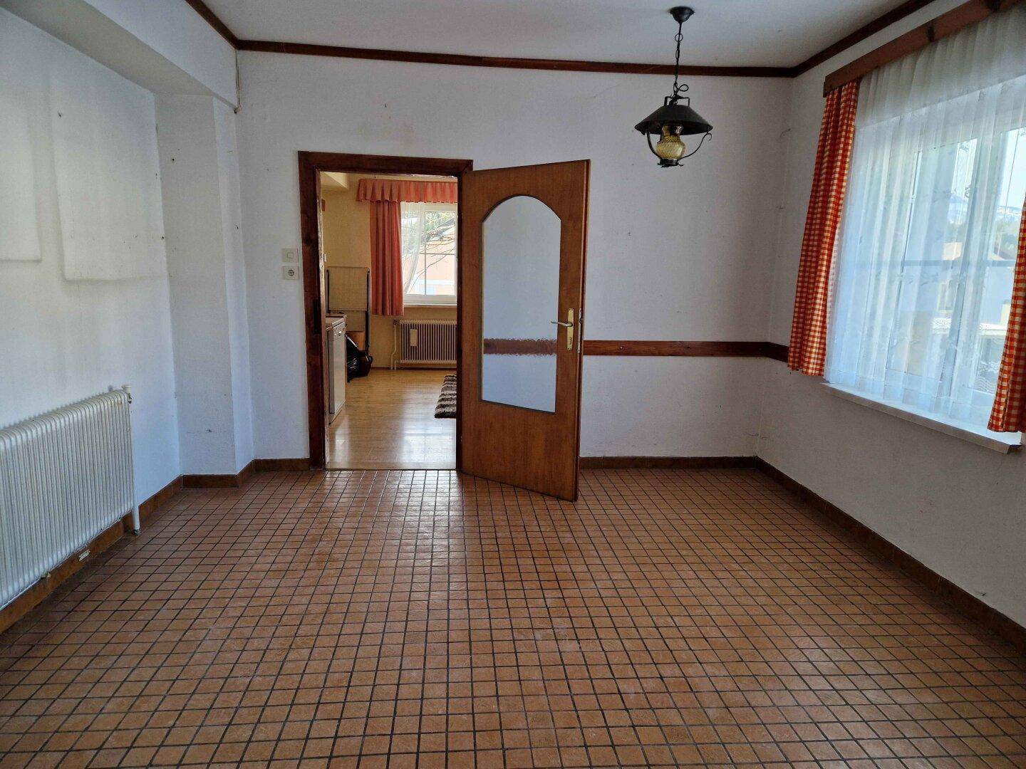 Leerer Raum mit kariertem Fliesenboden und Fenster mit karierten Vorhängen.