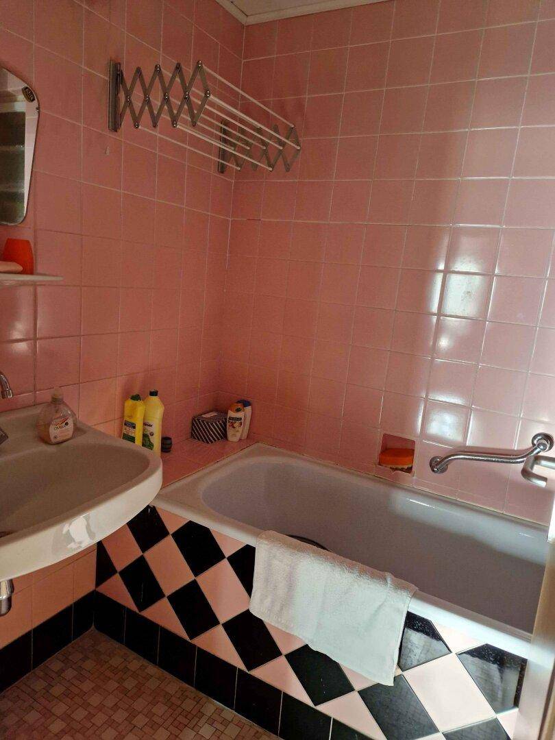 Badezimmer im 80er-Jahre-Stil mit rosa Fliesen und schwarz-weißem Schachbrettmuster.