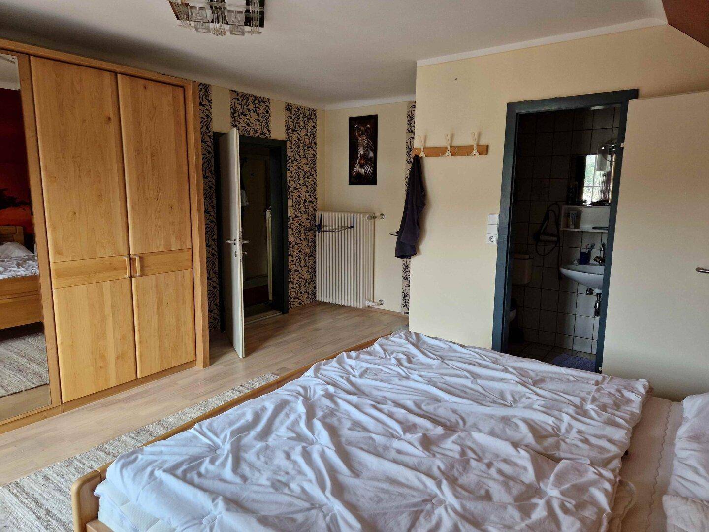 Schlafzimmer mit großem Kleiderschrank und direktem Zugang zu einem kleinen Badezimmer.
