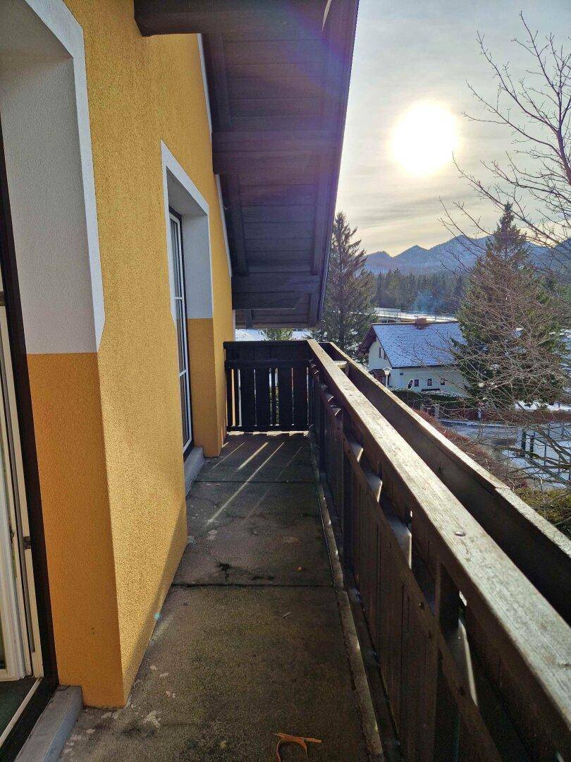 Schmaler Balkon mit Holzbalkonbrüstung und Blick auf verschneite Berge und umliegende Häuser.