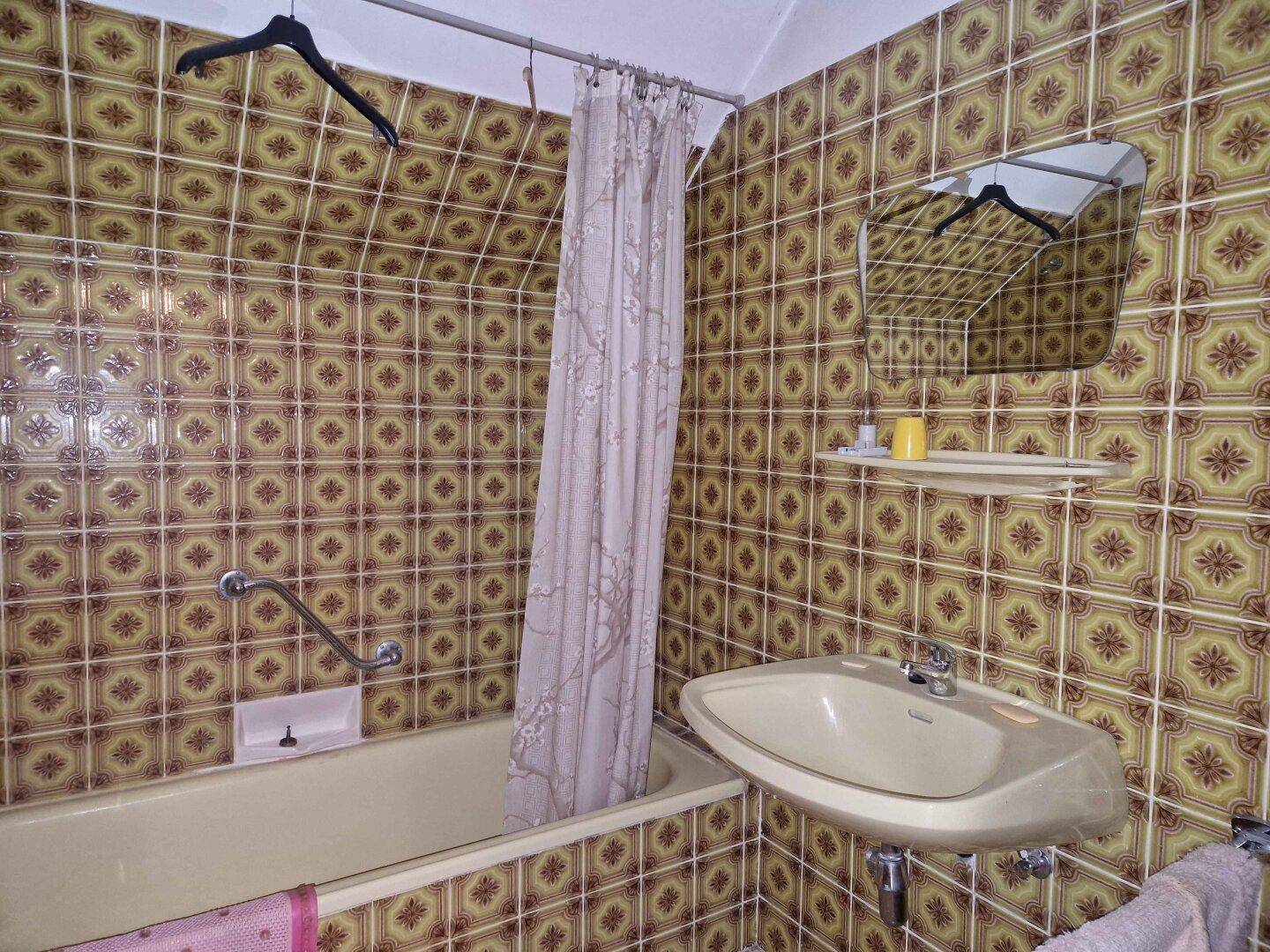 Badezimmer mit Badewanne, Waschbecken und gemusterten Fliesen im Retro-Stil.