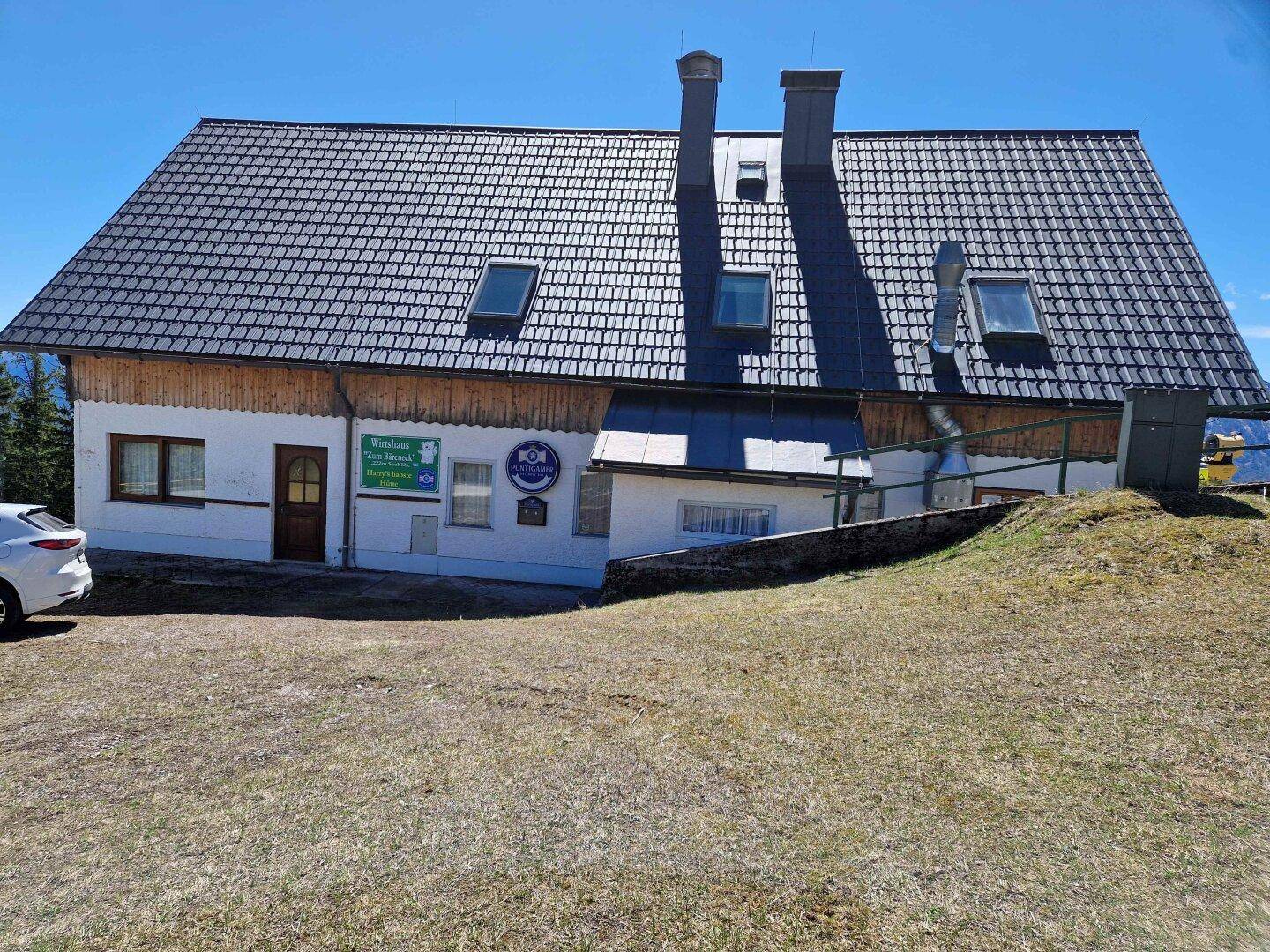 Rückseite eines alpinen Gebäudes mit dunklem Ziegeldach und mehreren Dachfenstern.
