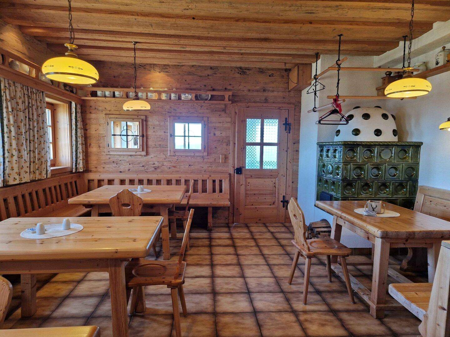 Gemütlicher Essbereich mit Holztischen, Bänken und einem traditionellen Kachelofen.