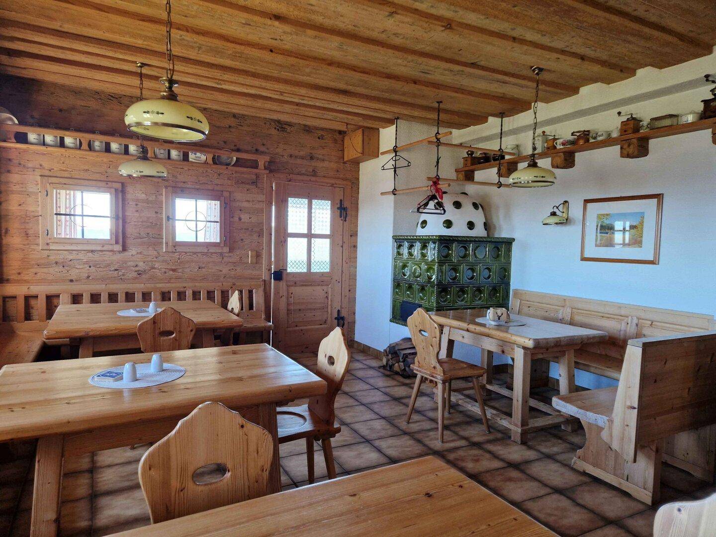 Traditioneller Essbereich mit Holzeinrichtung, Kachelofen und Blick auf die umliegende Landschaft.