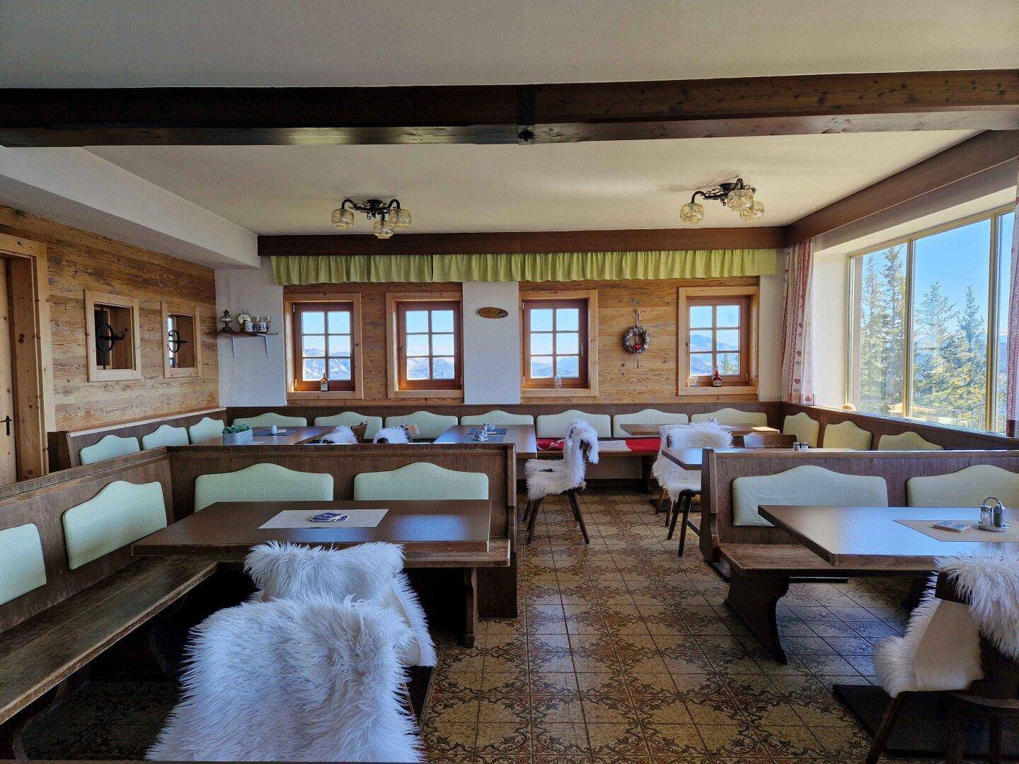 Gemütlicher Speisesaal im alpinen Stil mit Holzbänken, Tischen und großen Fenstern mit Bergblick.