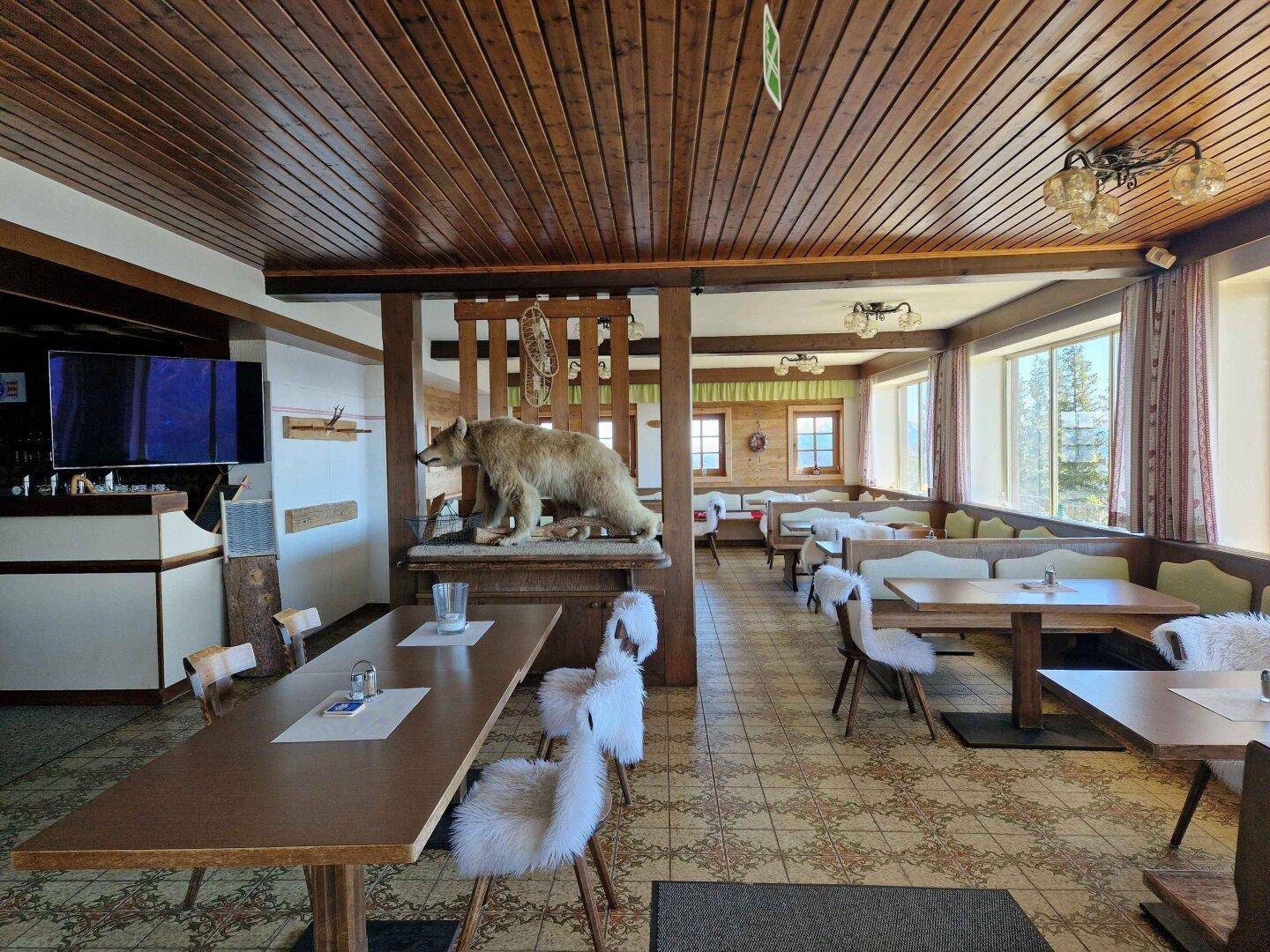 Rustikaler Speisesaal mit Holzdecke, traditionellen Möbeln und einem ausgestopften Bären als Dekoration.