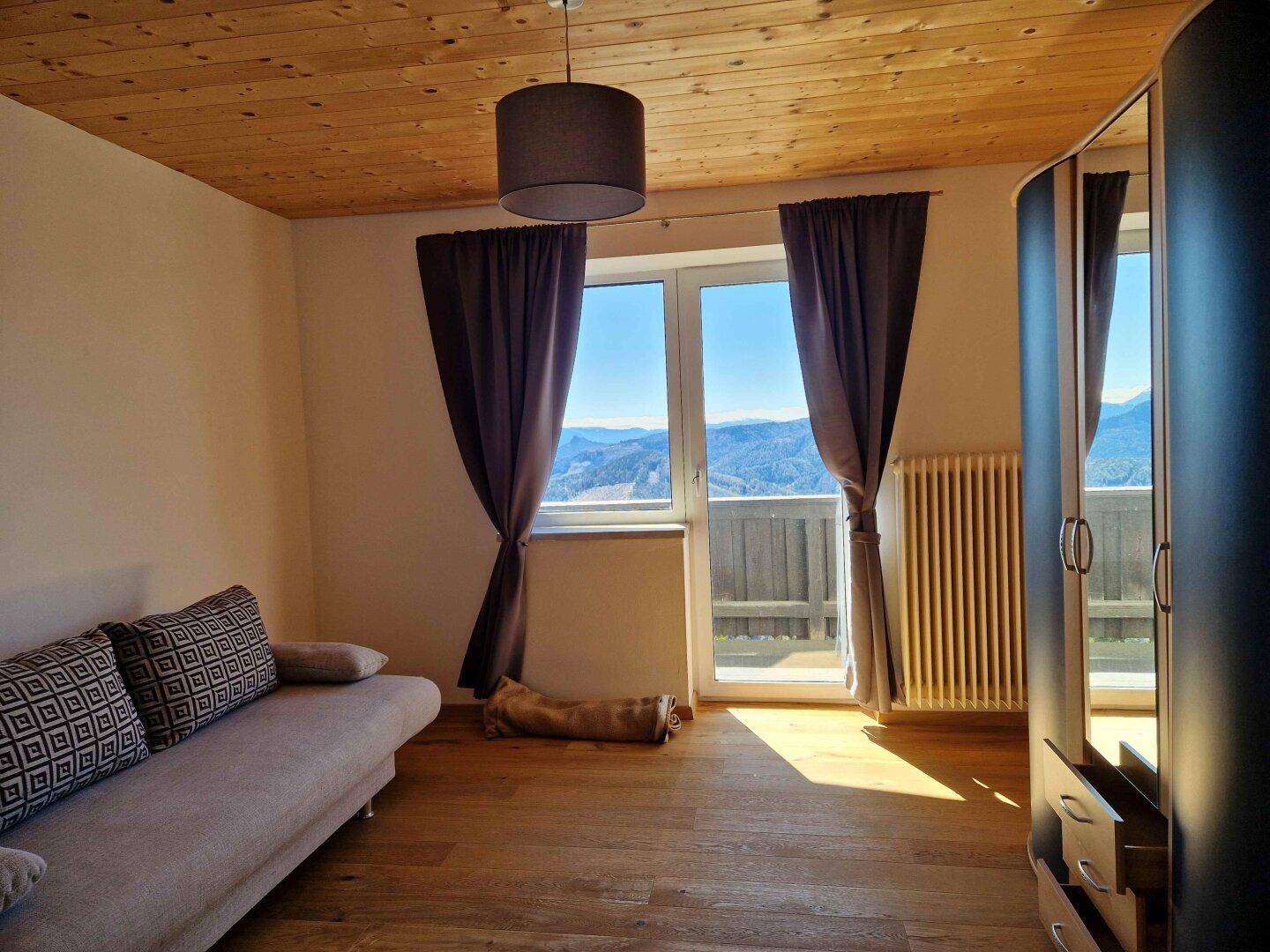 Schlafzimmer mit Holzboden, Balkonzugang und weitem Blick auf die Berglandschaft.