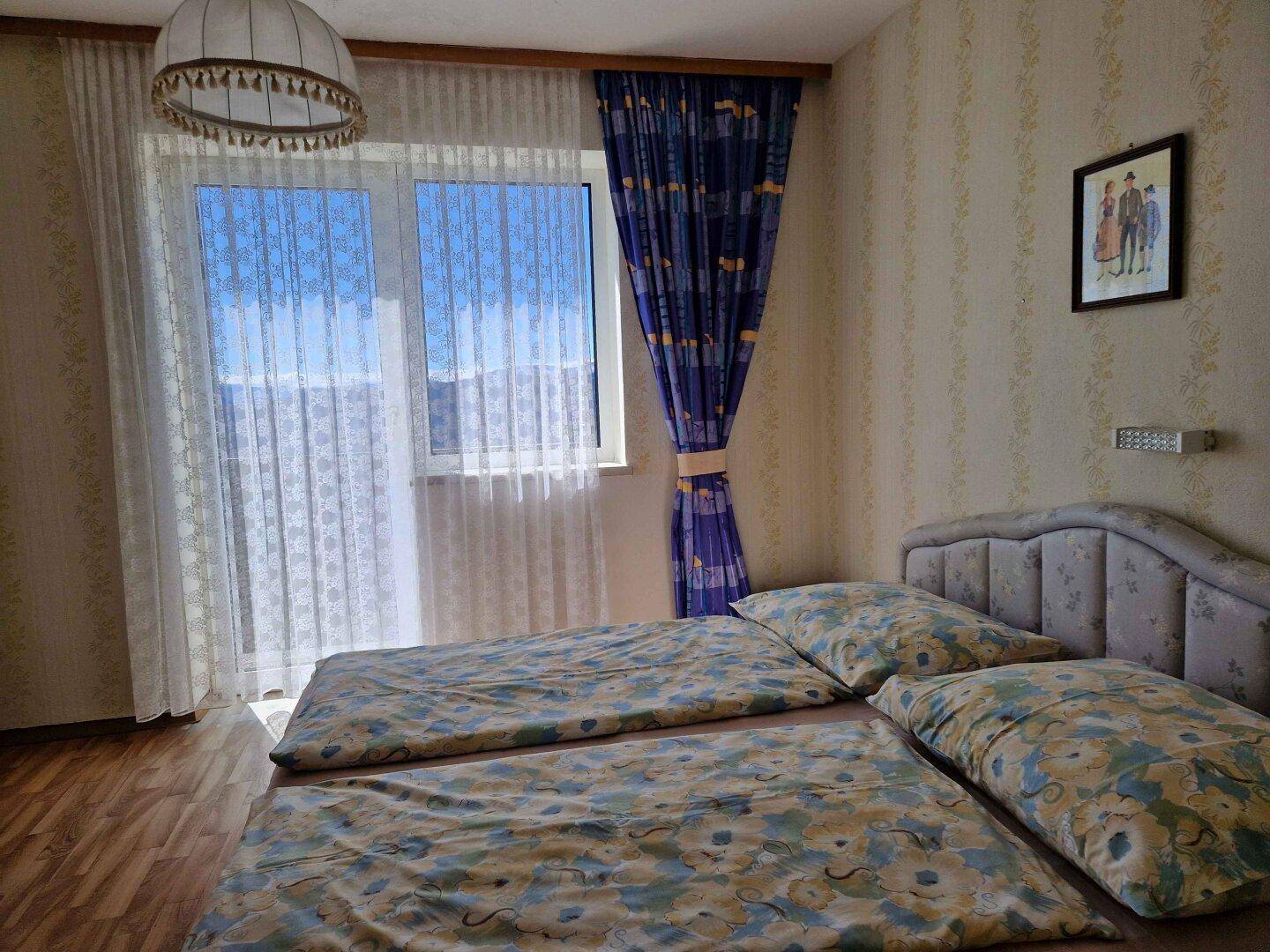 Schlafzimmer mit zwei Einzelbetten, Holzboden und Fenster mit Blick ins Grüne.