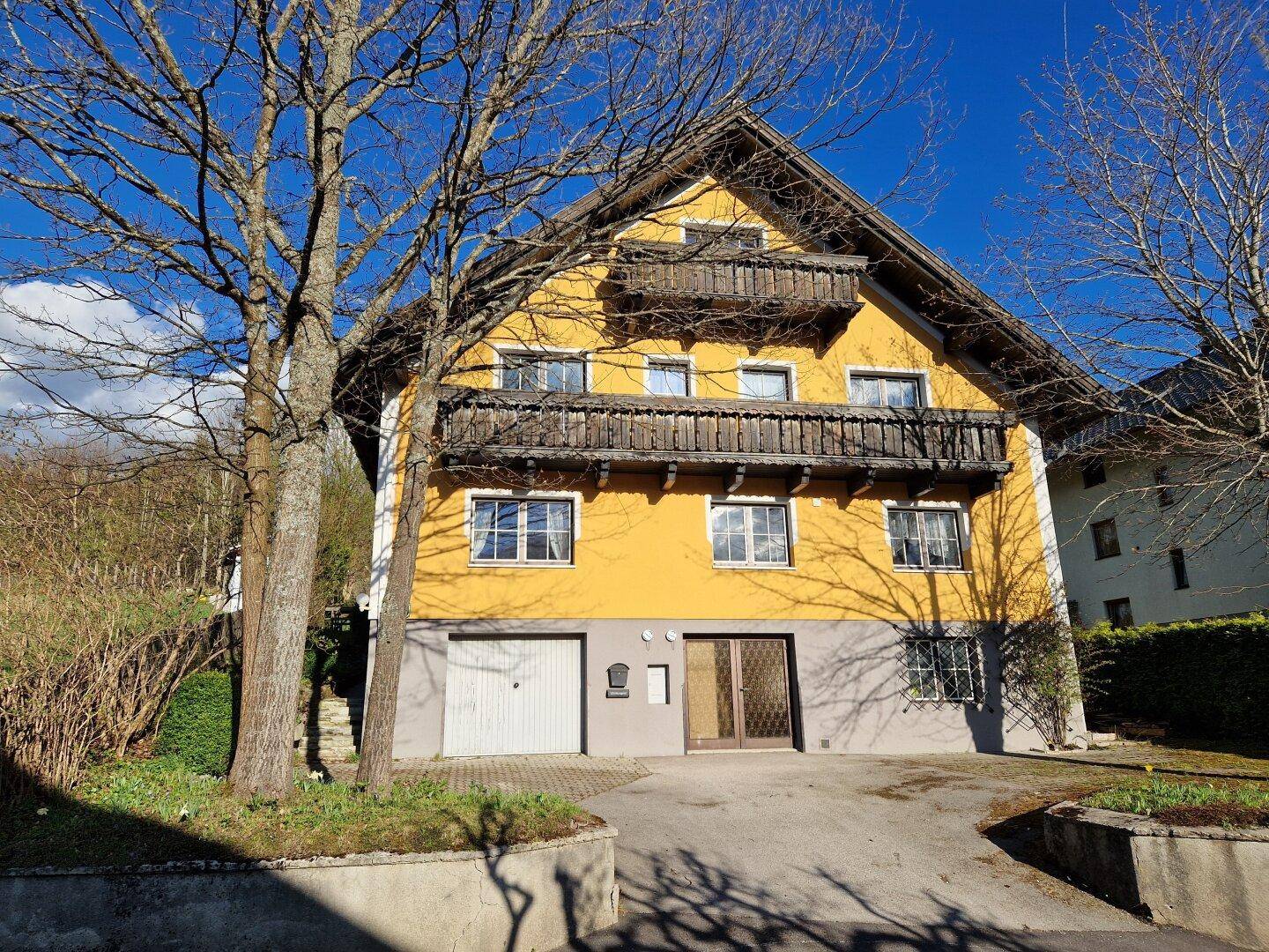 Traditionelles gelbes Haus mit mehreren Holzbalkonen, Satteldach und integrierter Garage.
