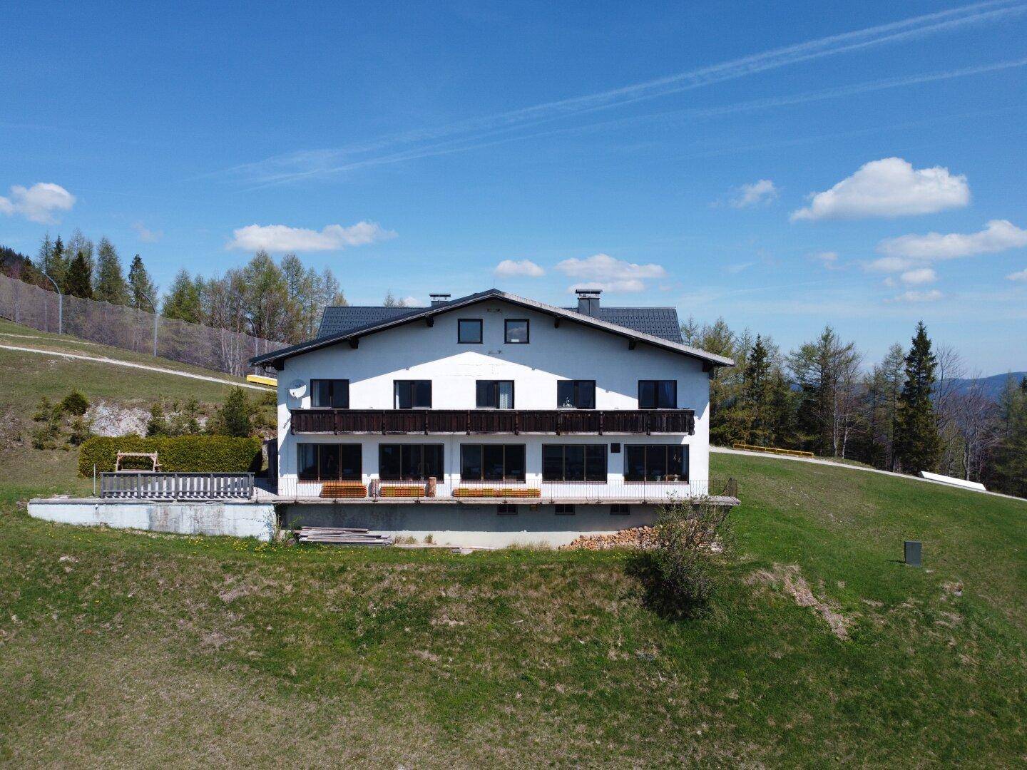 Vorderansicht des Gebäudes mit Balkonen, großen Fenstern und einer grünen Wiese im Vordergrund.