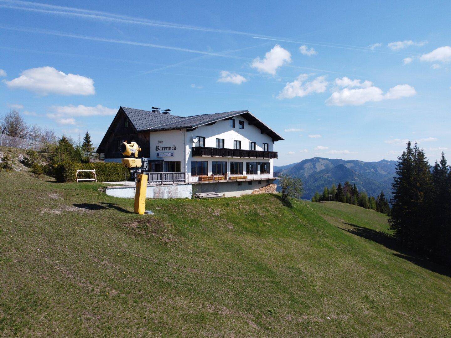 Gebäude im alpinen Stil auf einem Hügel mit Balkonen und weitem Blick auf die Berglandschaft.