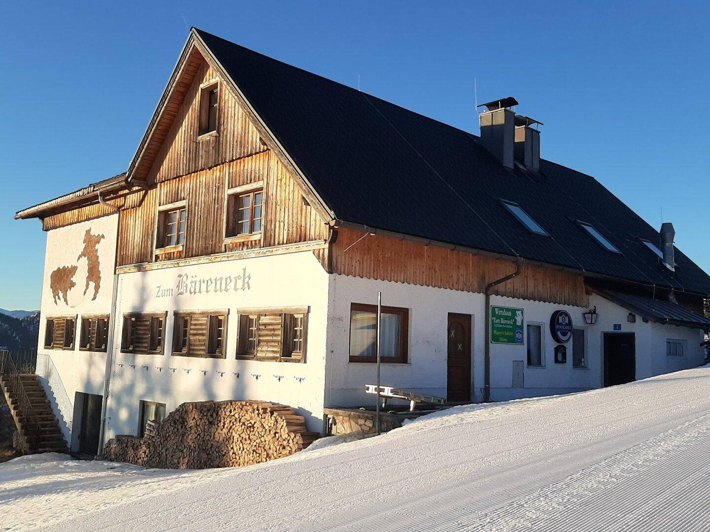 Alpines Gebäude im Winter, umgeben von Schnee, mit Holzelementen und einem dunklen Dach.