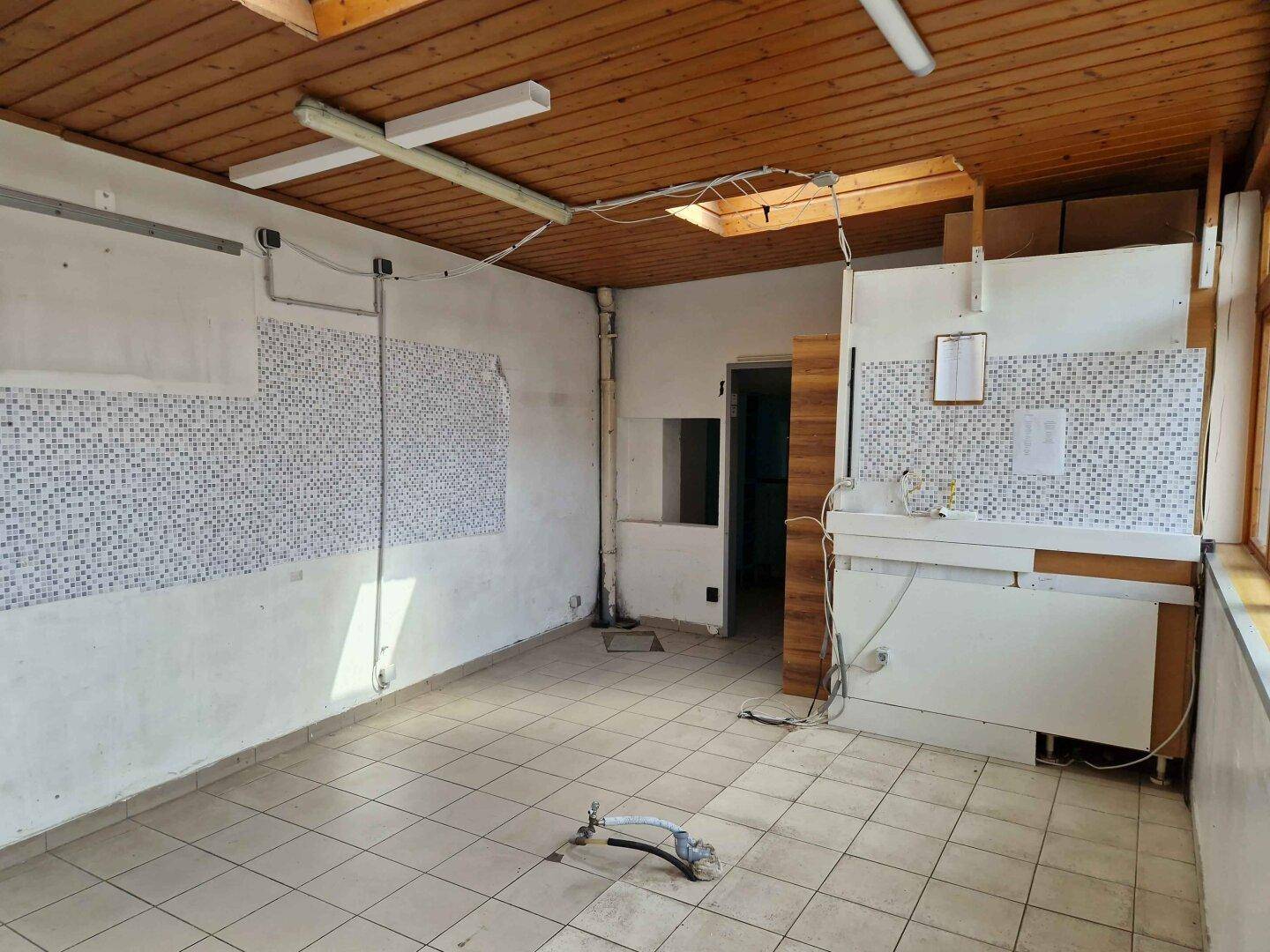 Leerer Raum mit Holzdach, Fliesenboden und Spülbereich, bereit zur Renovierung und Neugestaltung.