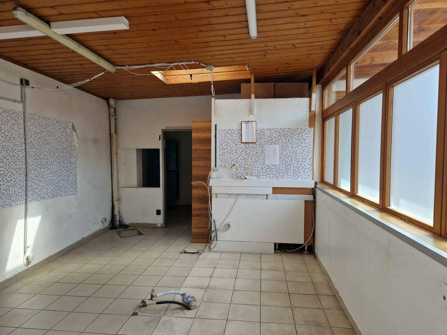 Geräumiger Raum mit Holzdach, Fliesenboden und großen Fenstern, ideal für einen Umbau.
