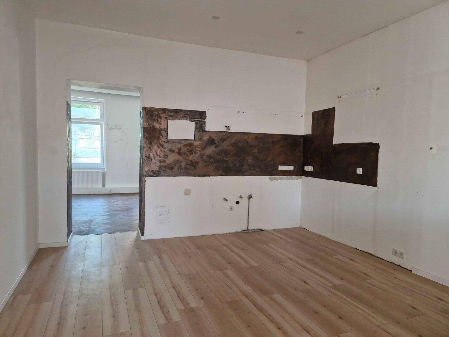 Leere Küche mit Holzboden und vorbereiteten Wandflächen, bereit für den Einbau neuer Elemente.