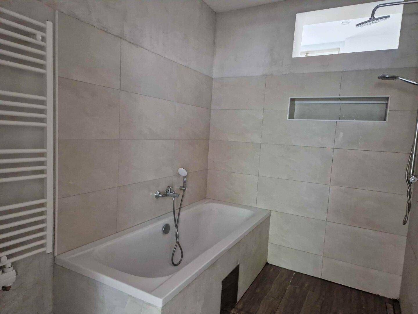 Modernes Badezimmer mit Badewanne, Duschbereich und beheiztem Handtuchhalter an der Wand.