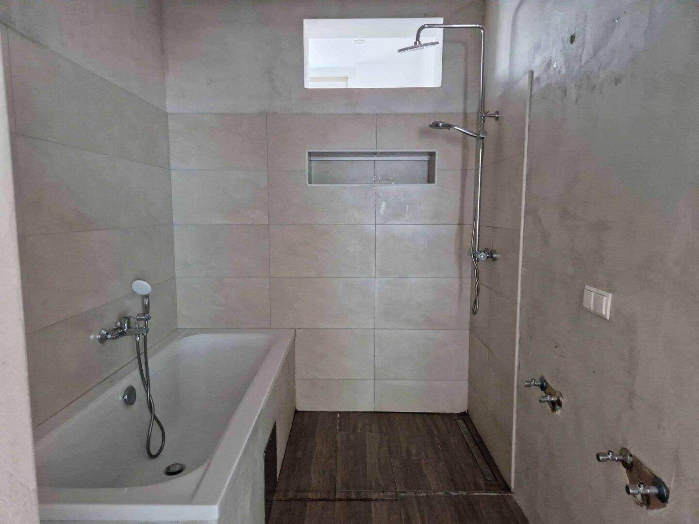 Helles Badezimmer mit Badewanne, Duschbereich und beigefarbenen Fliesen an den Wänden.