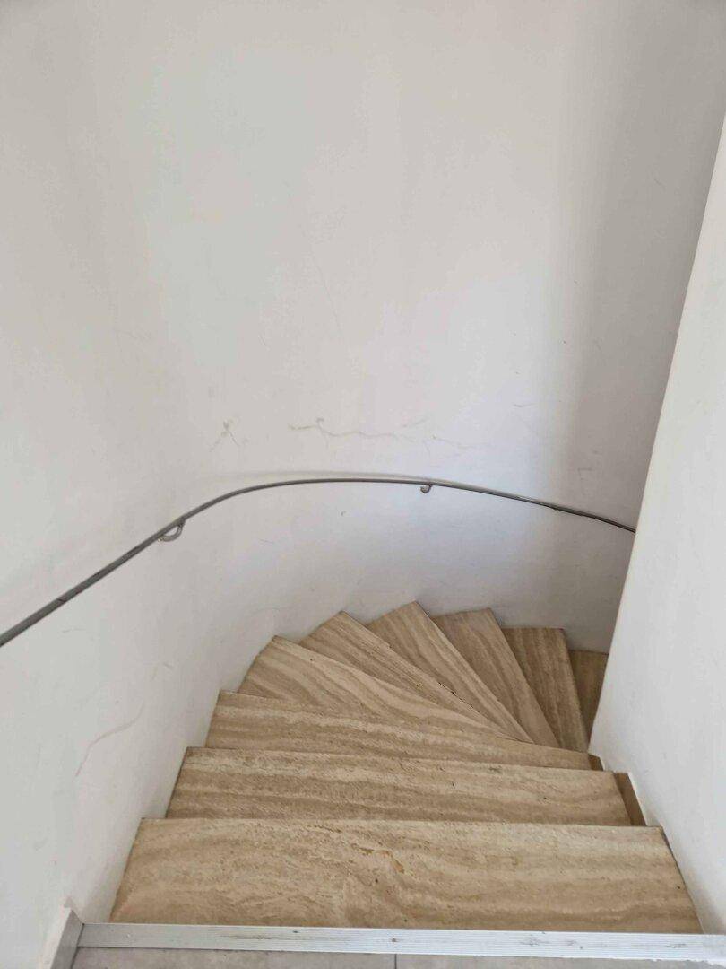 Wendeltreppe mit hellen Steinstufen und minimalistischem Handlauf, von oben gesehen.