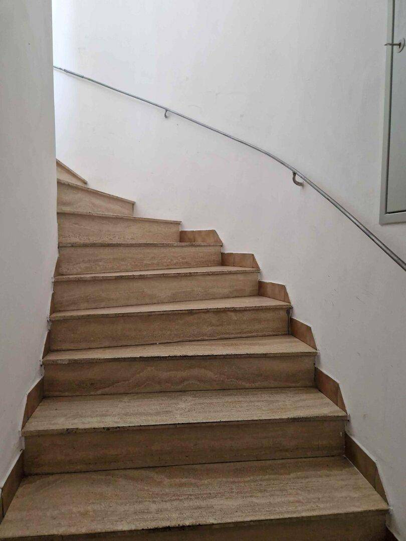 Treppenhaus mit hellen Steinstufen und einem schlichten Handlauf, gut beleuchtet.