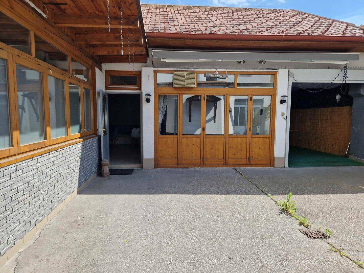 Gepflasterter Außenbereich mit Holztüren und Zugang zu einem Garagenbereich des Gebäudes.