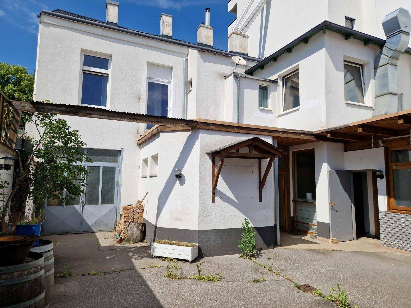 Hinterhofbereich eines weißen Gebäudes mit gepflastertem Boden und verschiedenen Zugängen.