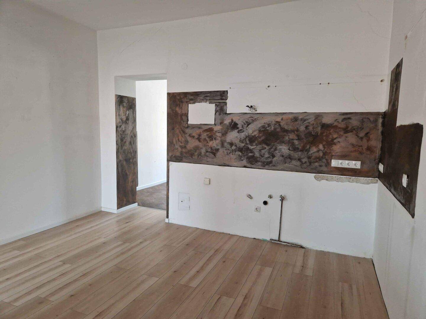 Heller Küchenraum mit Holzboden und unfertigen Wänden, wartet auf die endgültige Gestaltung.