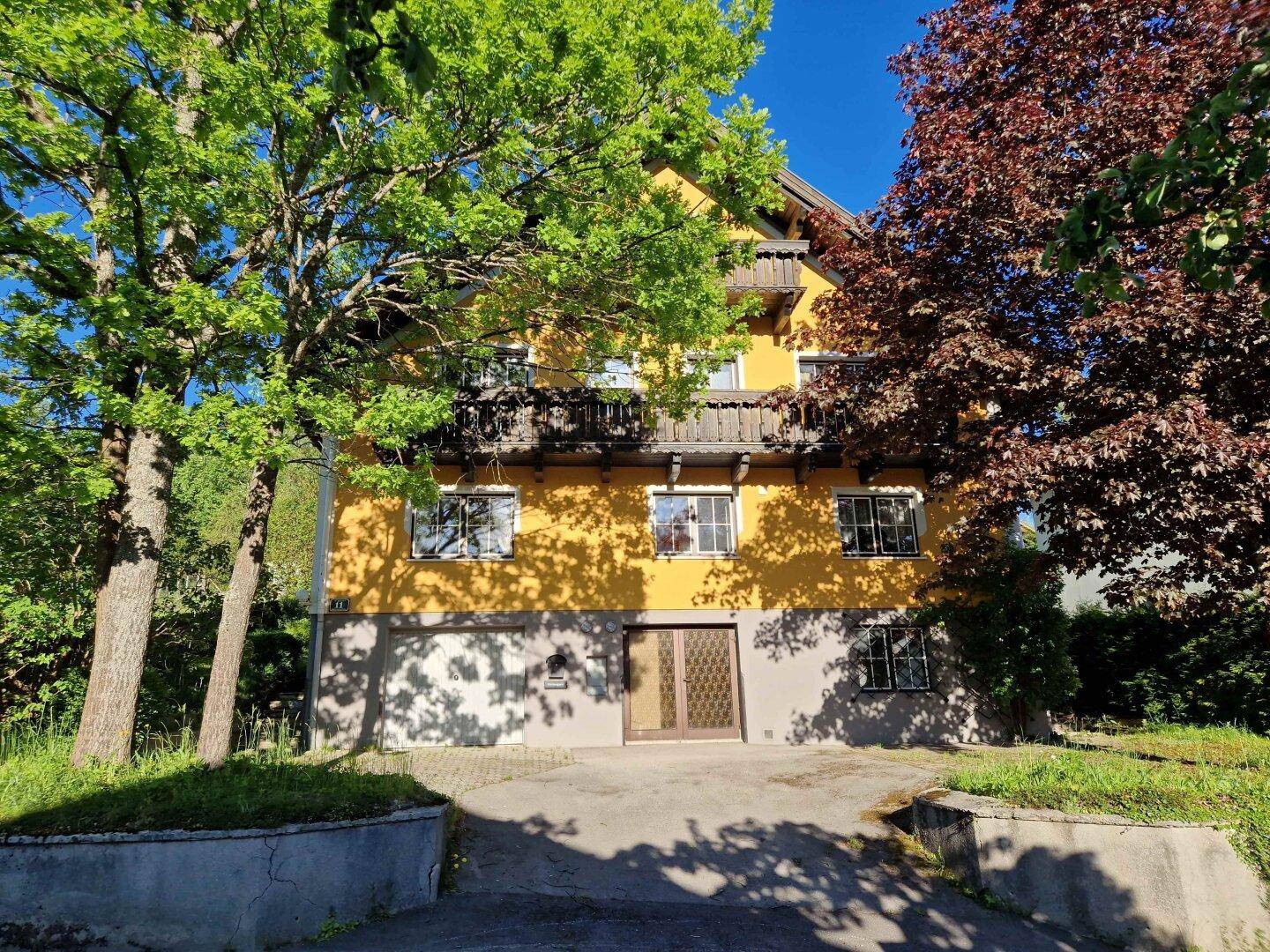 Traditionelles gelbes Haus mit Holzbalkonen und üppiger Vegetation im Sommer.