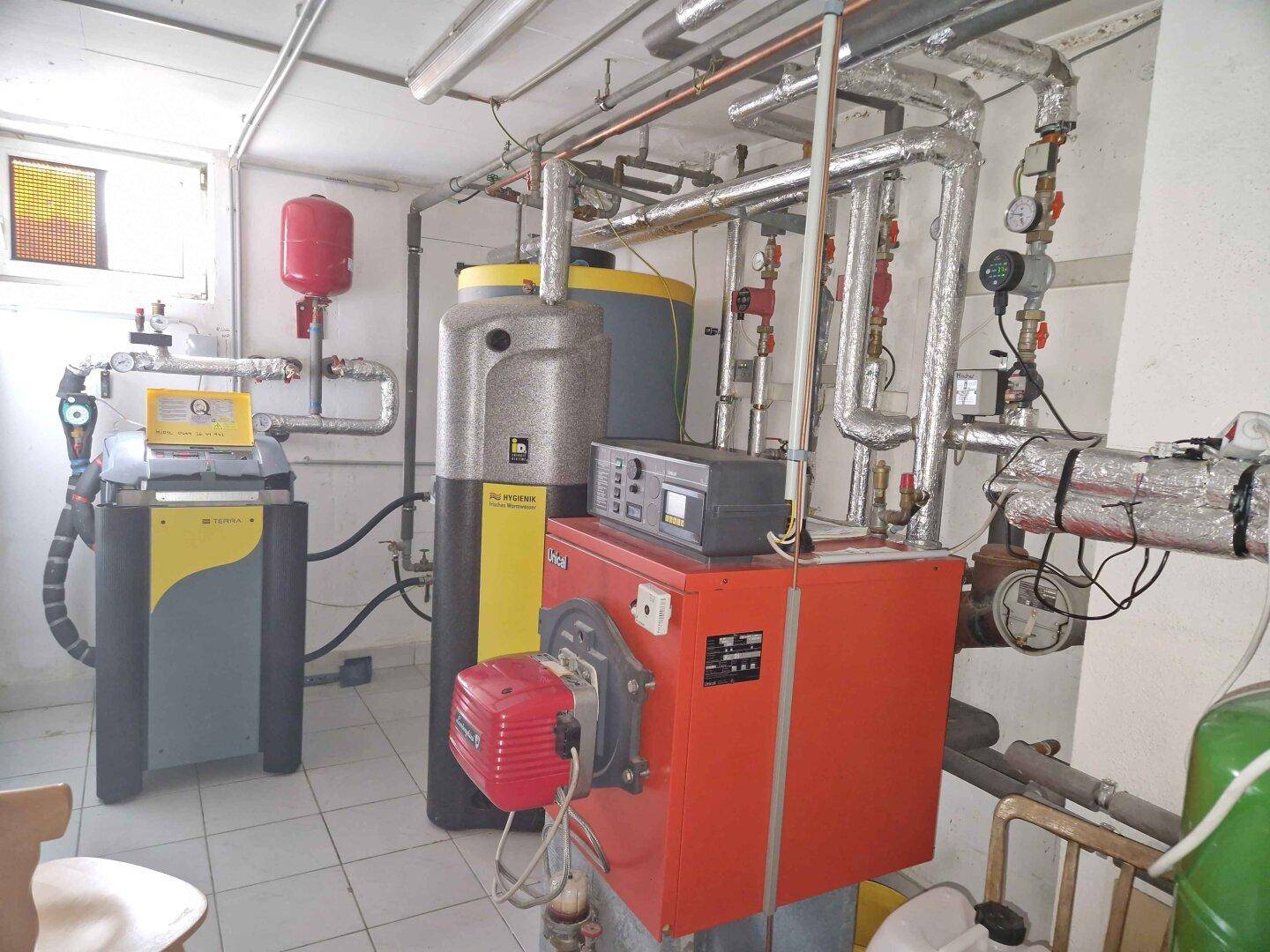 Heizungsraum im Keller mit moderner Heizungsanlage, Warmwasserspeicher und Rohrleitungen.