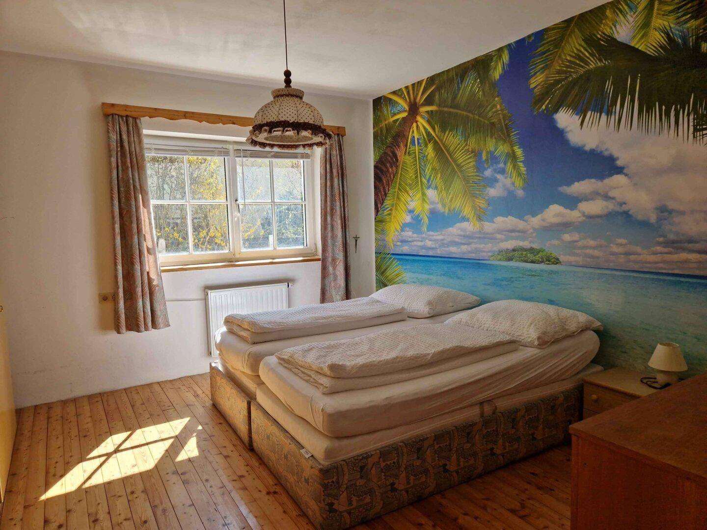 Schlafzimmer mit Doppelbett, Holzboden und einer auffälligen tropischen Wandtapete.