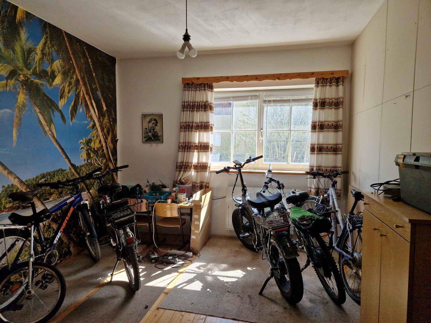 Geräumiges Zimmer mit Fenster, Holzboden und Stauraum, derzeit als Fahrradabstellraum genutzt.