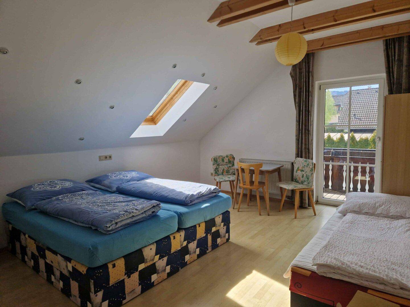 Dachgeschoss-Schlafzimmer mit zwei Betten, Dachfenster und Zugang zu einem kleinen Balkon.
