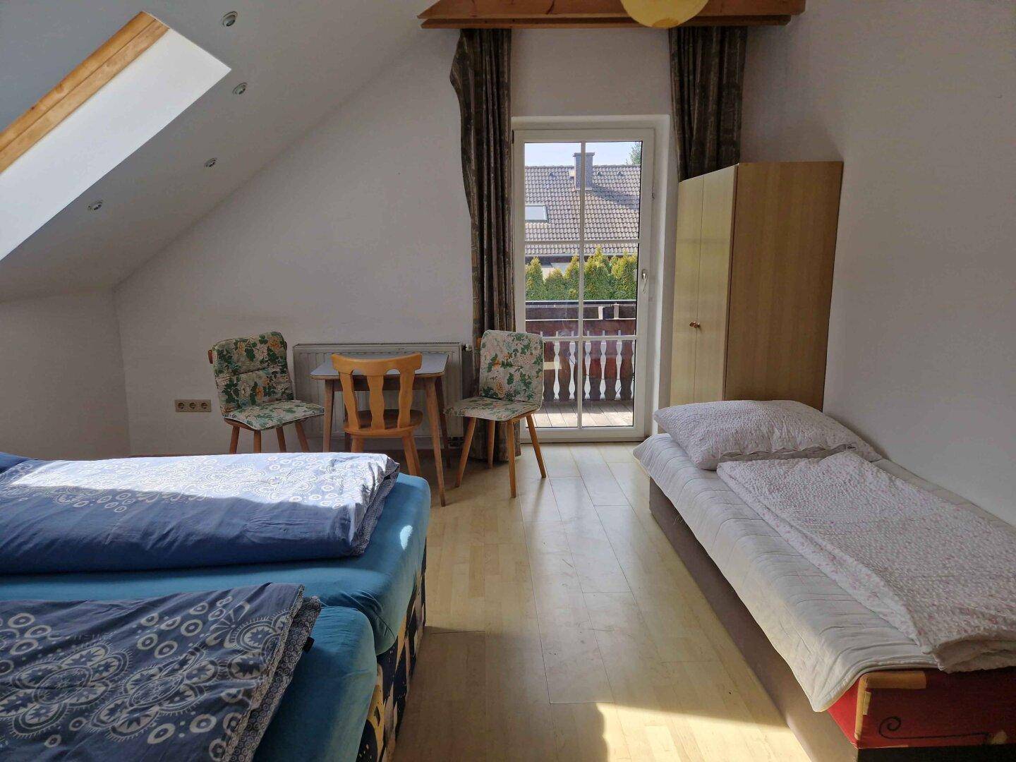 Helles Dachgeschoss-Schlafzimmer mit Einzelbett, Doppelbett und Balkontür.