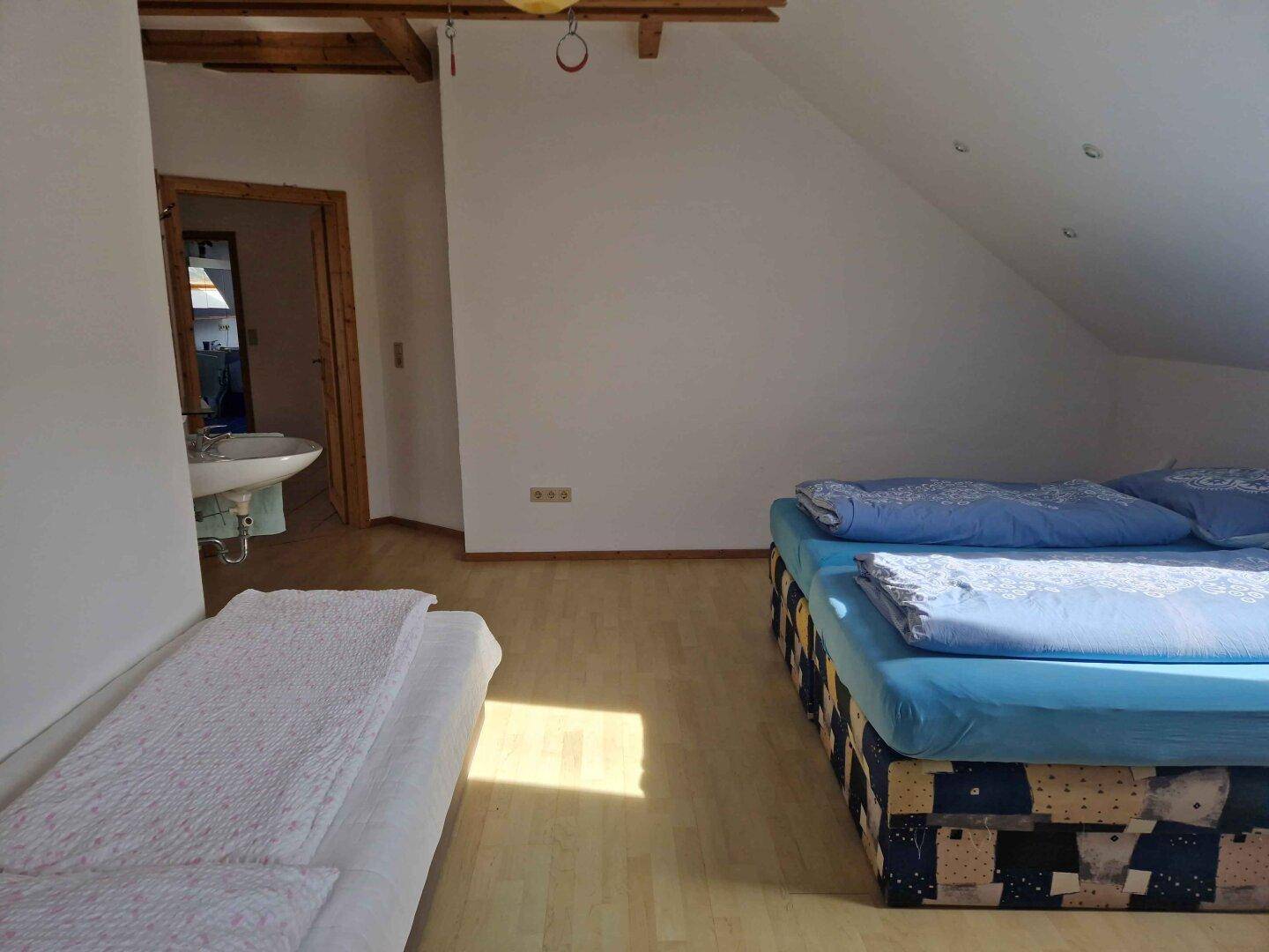 Dachgeschoss-Schlafzimmer mit Betten und Blick auf ein kleines Waschbecken im Raum.