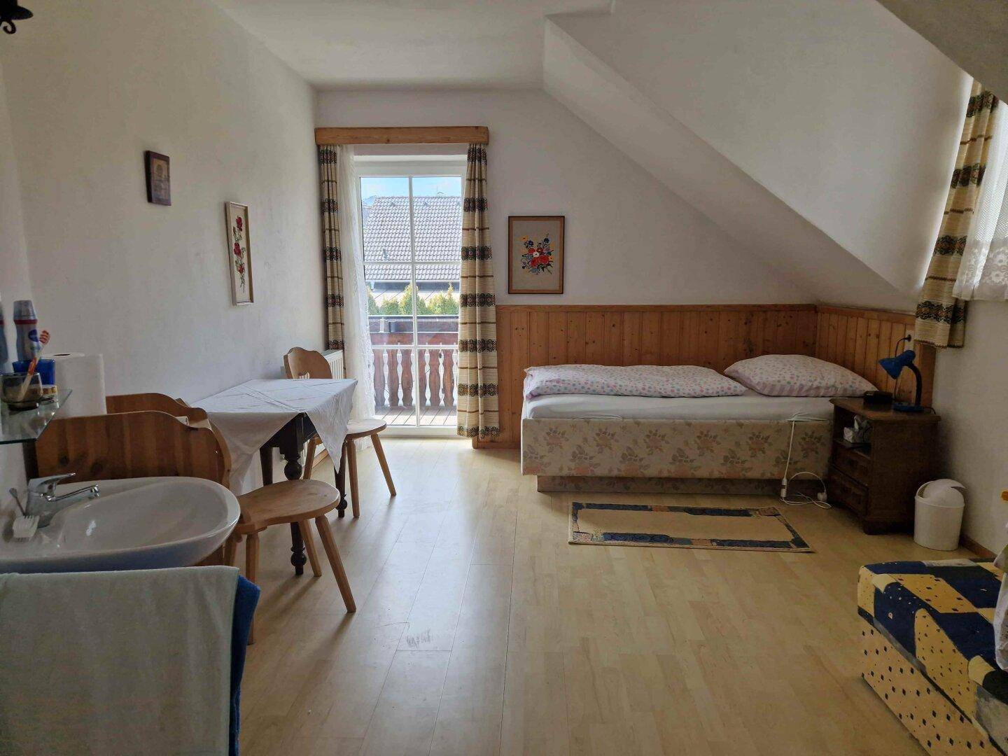 Gemütliches Dachgeschoss-Schlafzimmer mit Einzelbett, Waschbecken und Balkonzugang.