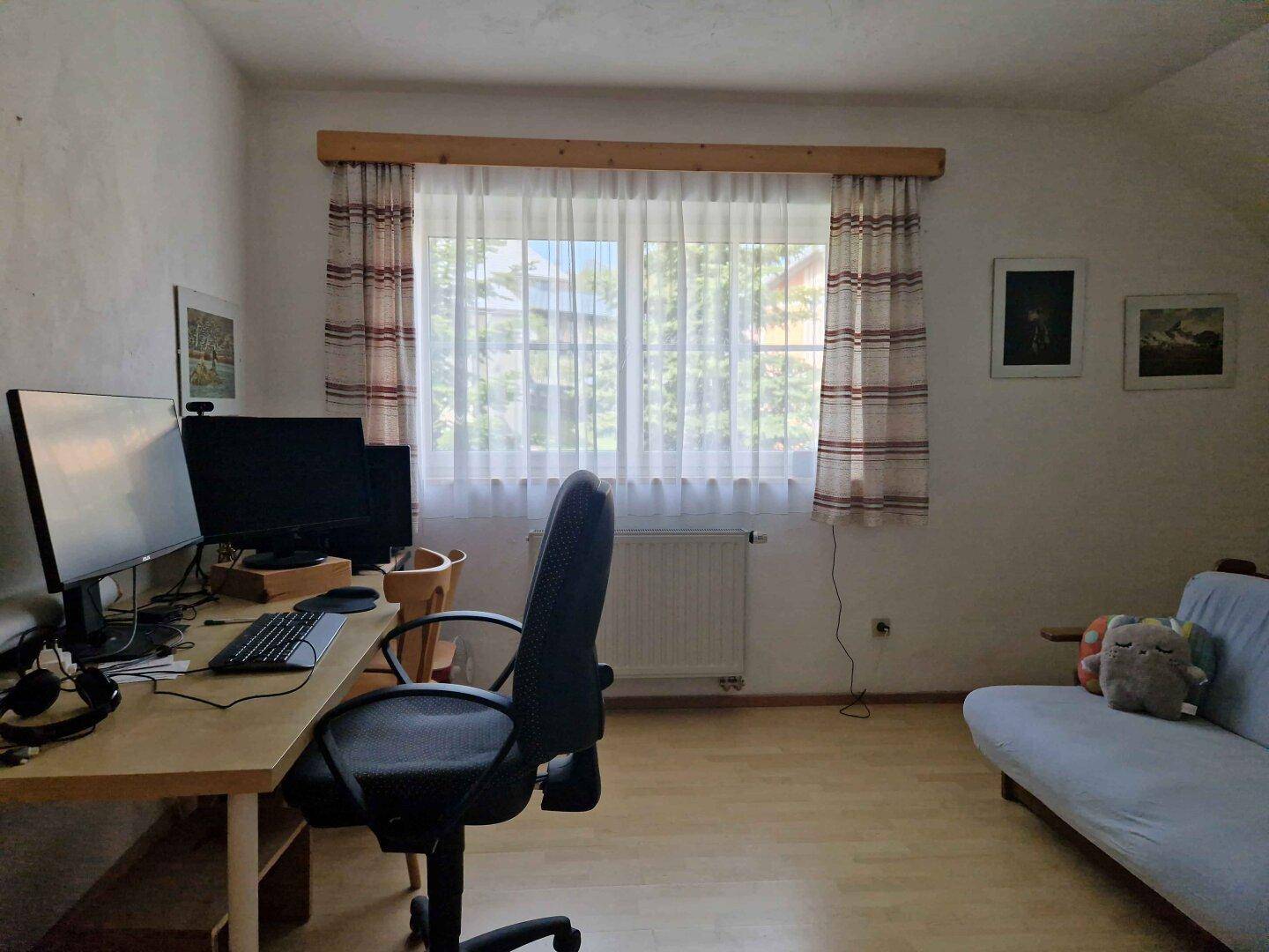 Dachgeschoss-Büro mit Schreibtisch, Computern und Fenster mit Blick ins Grüne.