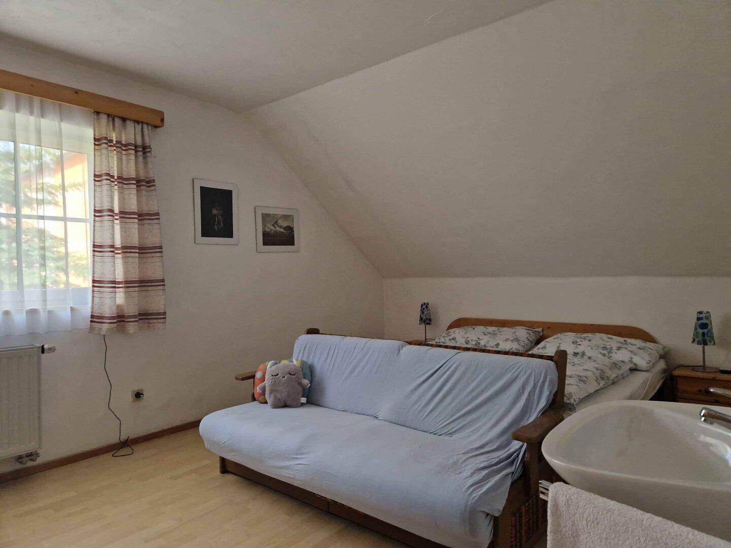 Dachgeschoss-Schlafzimmer mit Schlafsofa, Bett und integriertem Waschbecken.