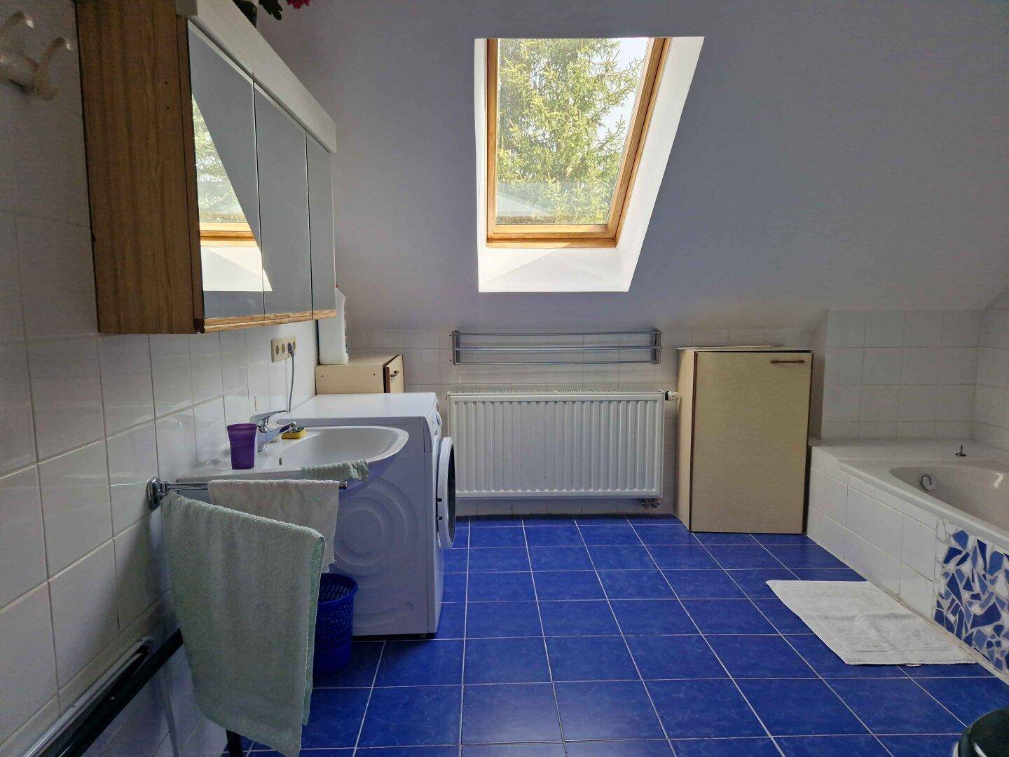Geräumiges Badezimmer im Dachgeschoss mit blauen Fliesen, Badewanne und Waschmaschine.