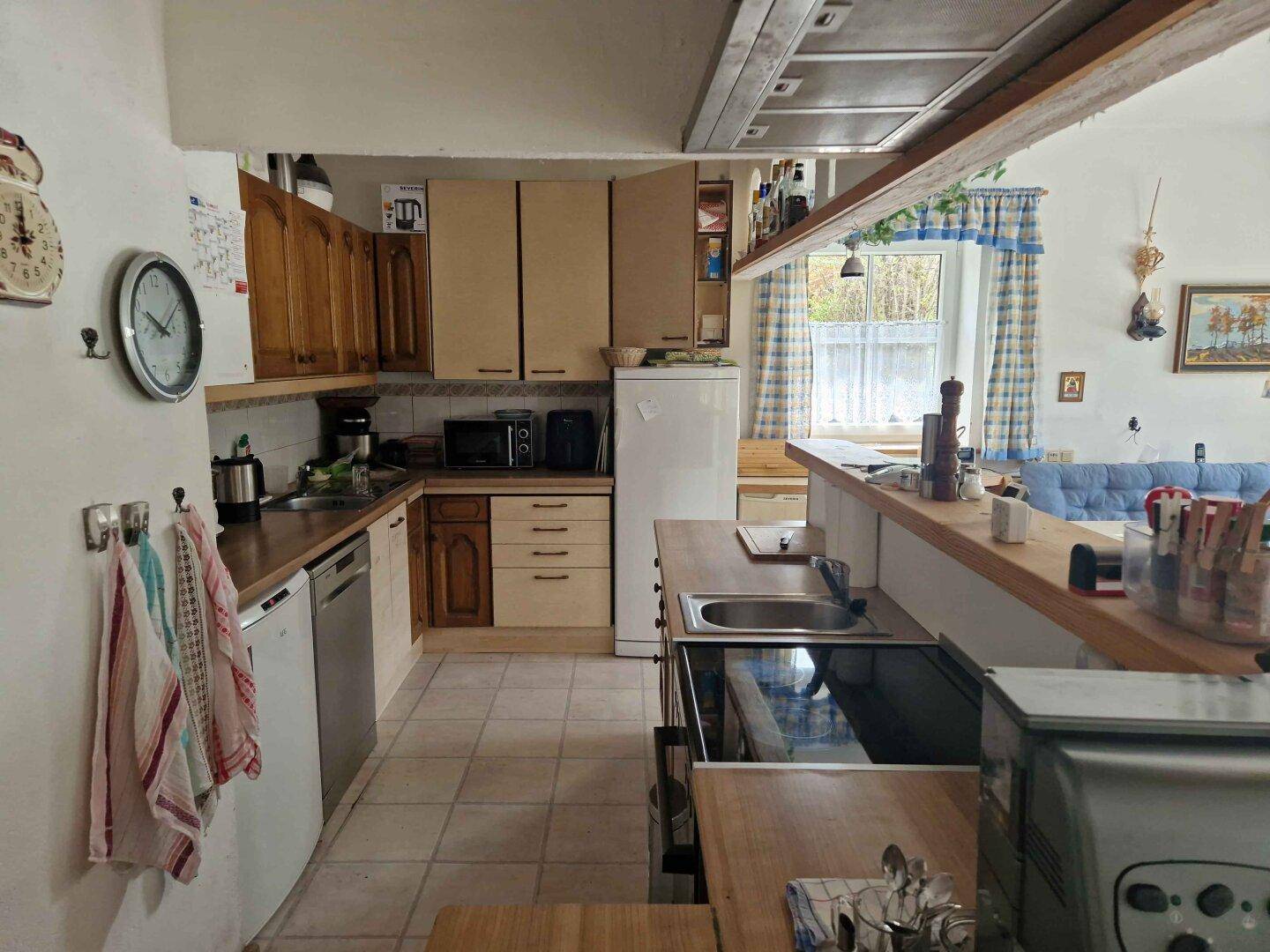 Funktionale Küche mit Holzschränken, Fliesenboden und Blick auf den Essbereich.