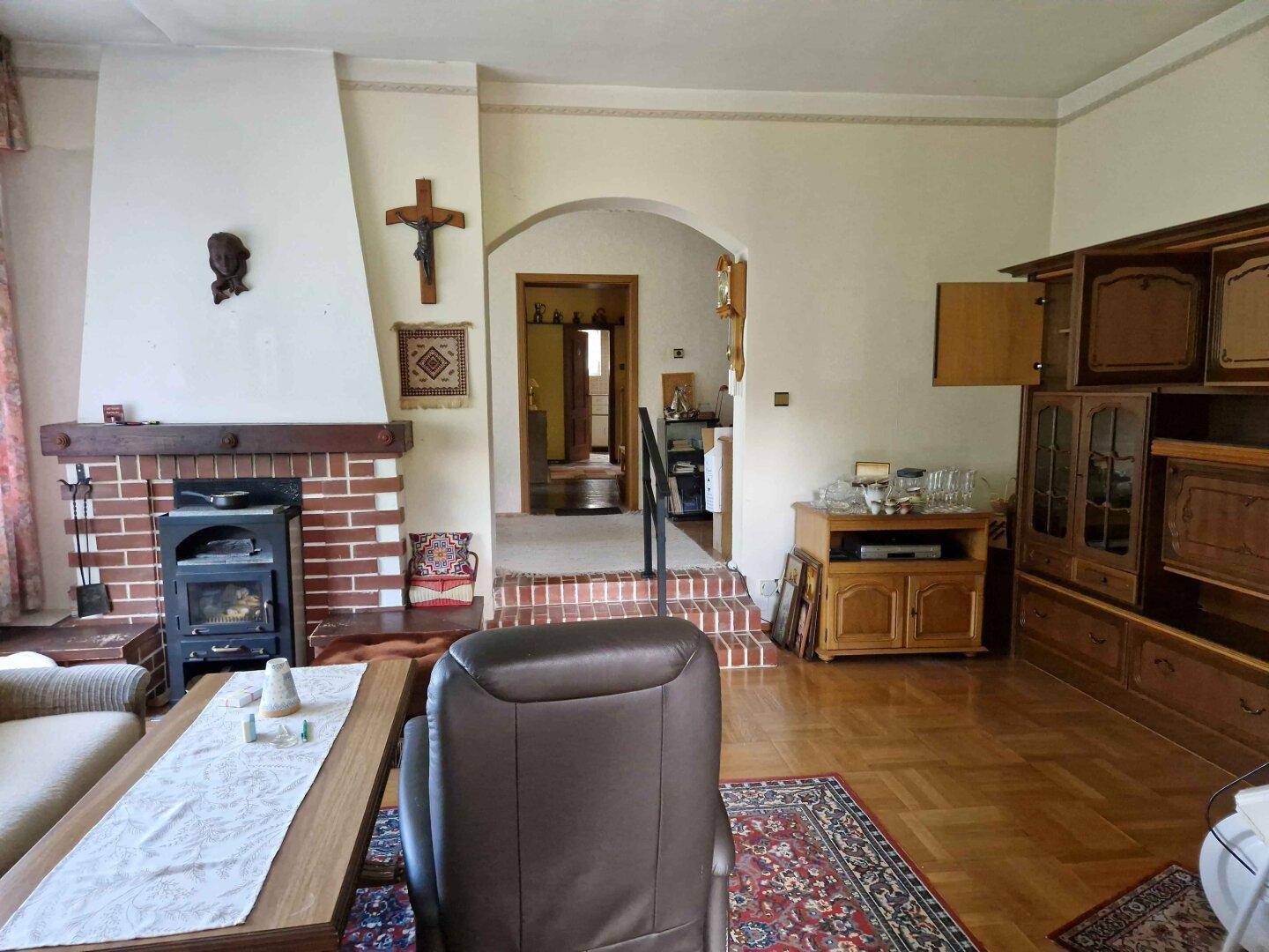 Traditionelles Wohnzimmer mit Kamin, Holzmöbeln und Parkettboden, einladender Übergang zu weiteren Räumen.