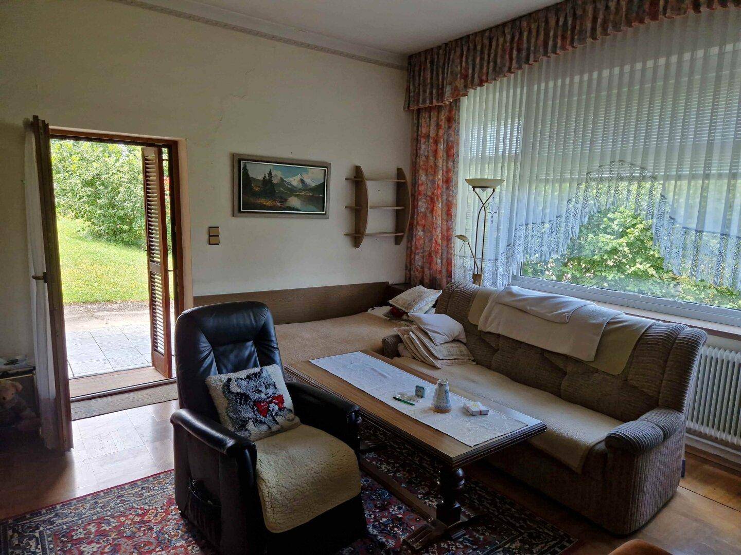 Gemütliches Wohnzimmer mit Sofa, Sessel und großem Fenster mit Blick ins Grüne, direkter Zugang zum Garten.