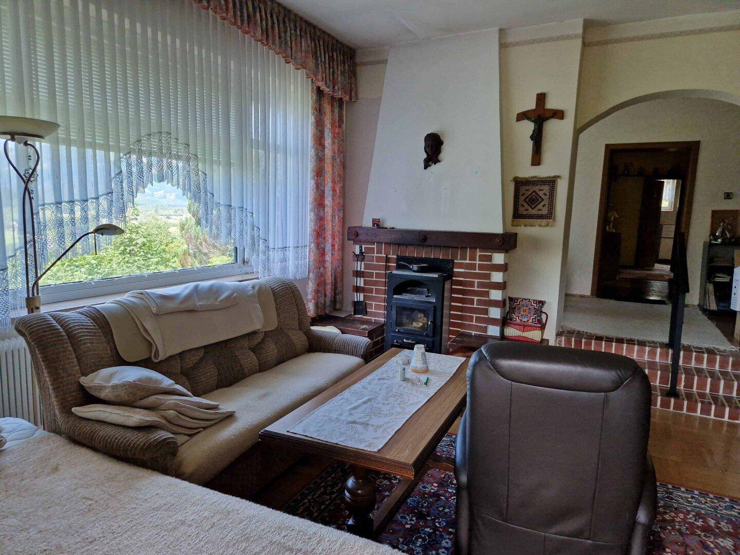 Helles Wohnzimmer mit Kamin, bequemen Sitzmöbeln und großem Fenster, das viel Tageslicht hereinlässt.