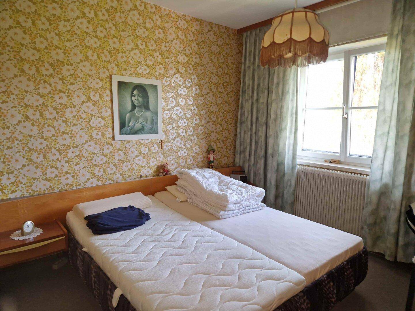 Gemütliches Schlafzimmer mit floraler Tapete, zwei Einzelbetten und einem Fenster, das viel Licht spendet.