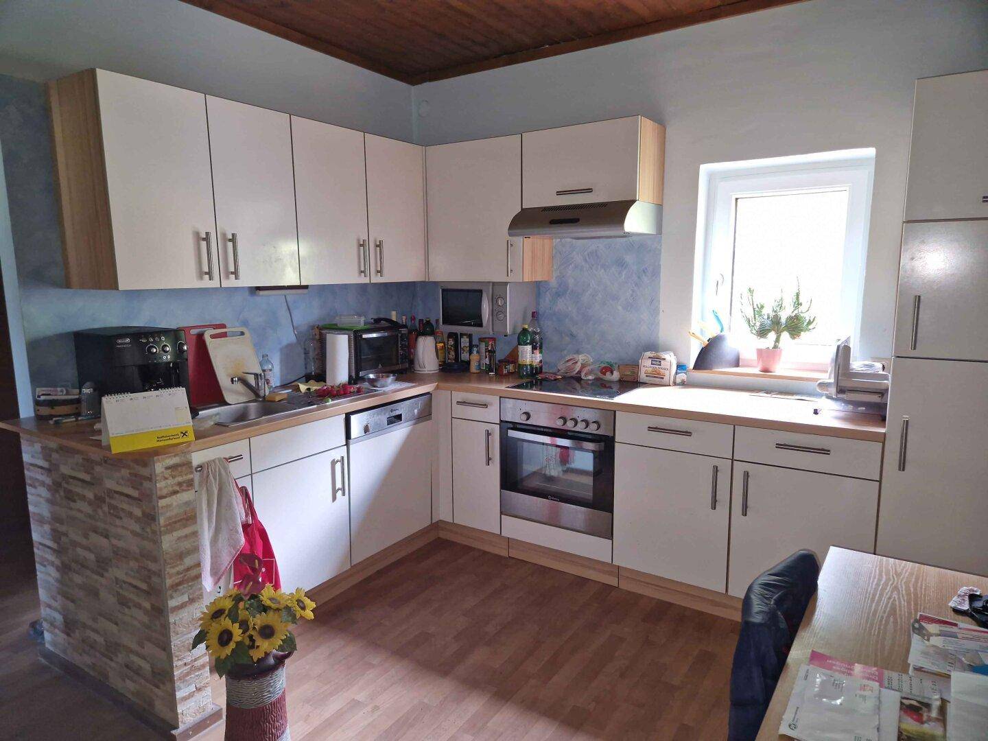 Moderne Küche mit weißen Schränken, Holzarbeitsplatten und blauer Akzentwand, ausgestattet mit Backofen und Geschirrspüler.