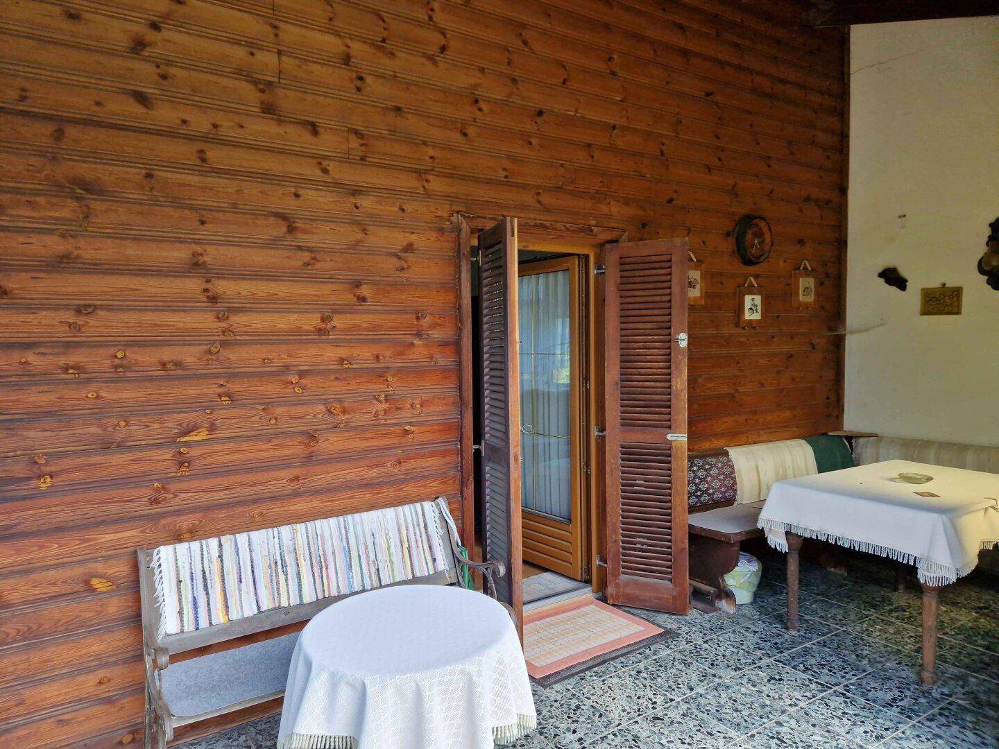 Überdachte Terrasse mit Holzwänden und gefliestem Boden, ideal für entspannte Stunden im Freien.
