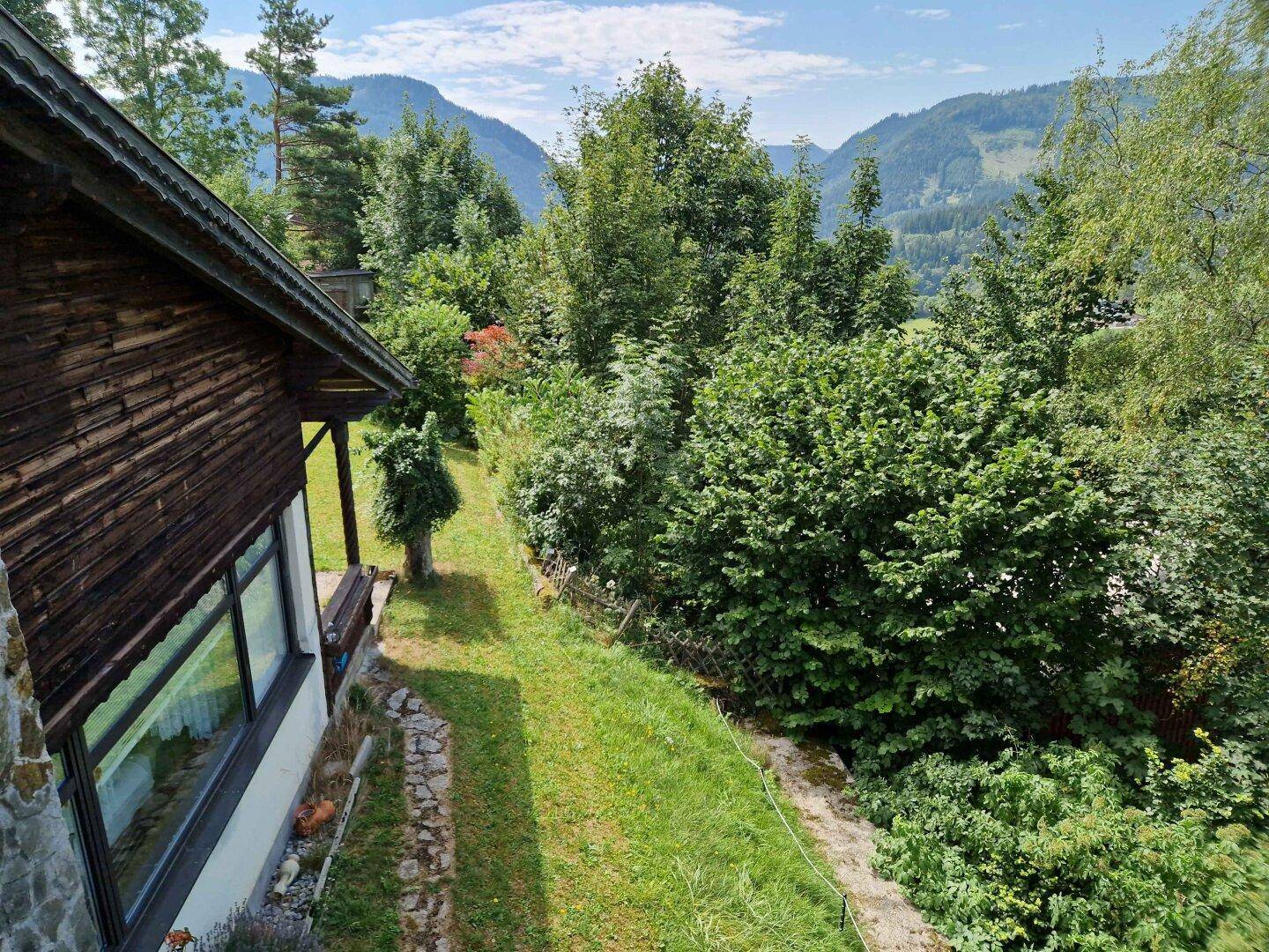 Seitenansicht des Hauses mit grüner Hanglage und weitem Blick auf die bewaldeten Berge und die Natur.
